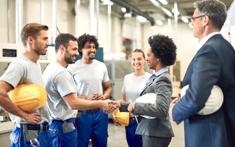 Happy African American manager greeting workers and handshaking with one of them in a factory.